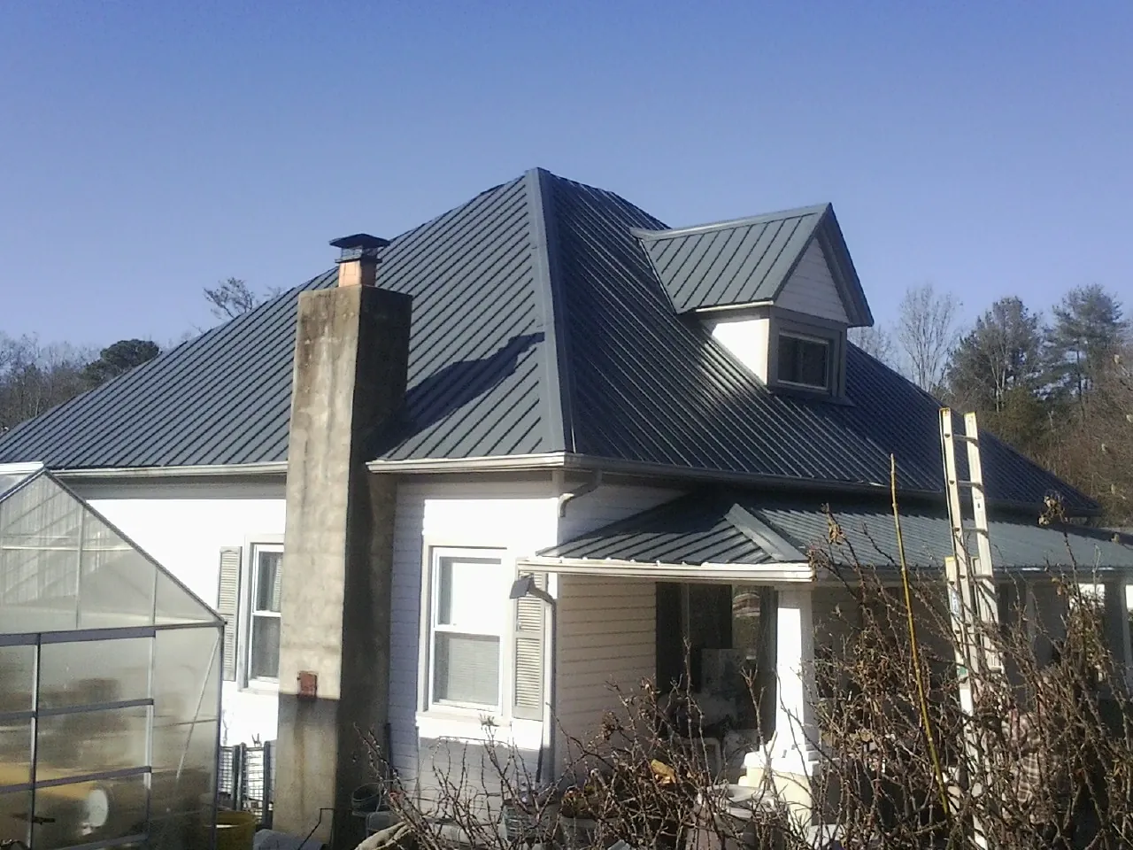 Dark blue standing seam metal roof on a white farmhouse with dormer — Slate & Tile Roof Repair by Roofing Brothers in Graham