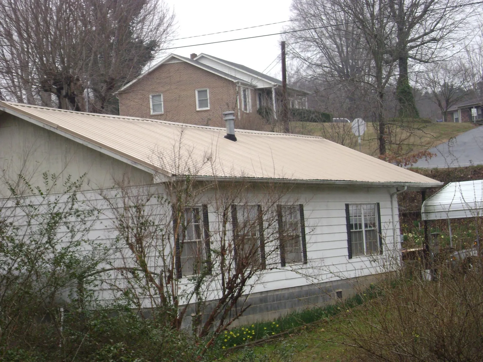 Tan metal roof on a white sided house set into a hillside — Commercial Roofing by Roofing Brothers in Graham
